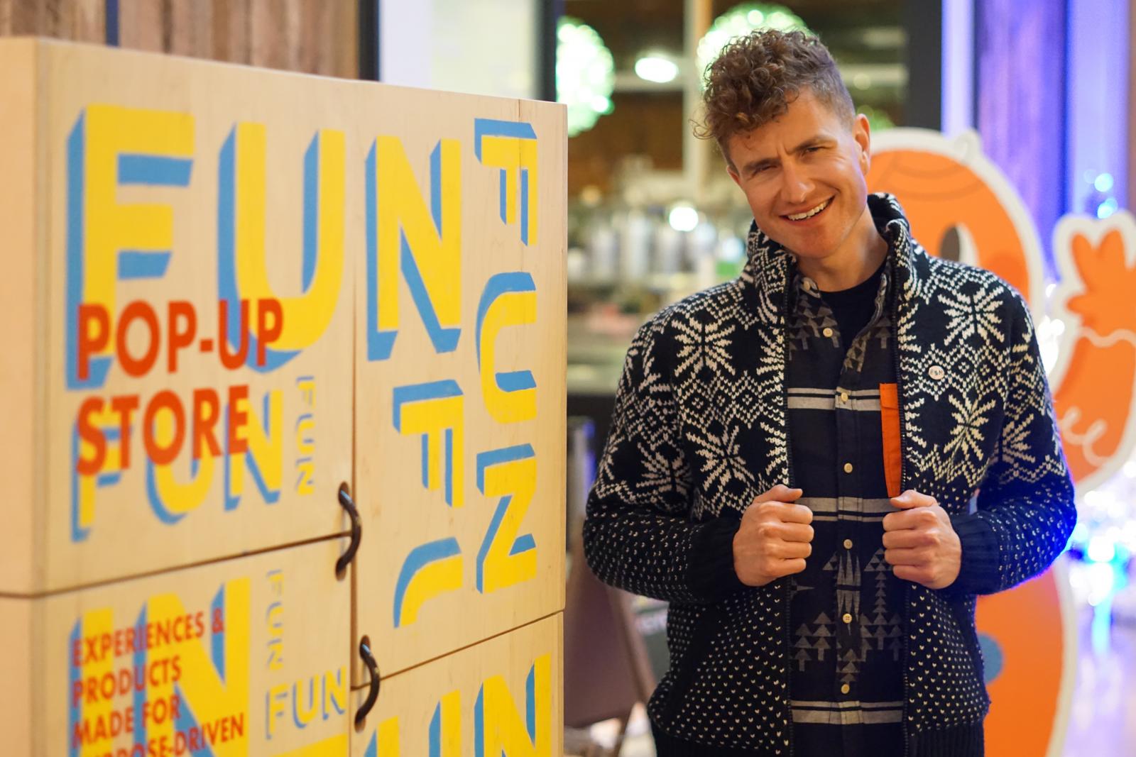 Personin cardigan stand by collage wall with words like "fun"