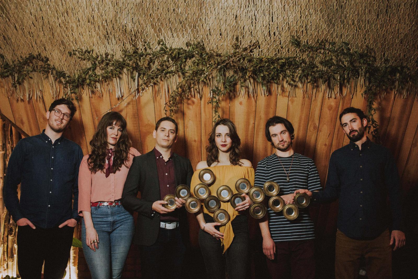 6 people line up in front of a fence with lush greenery. 