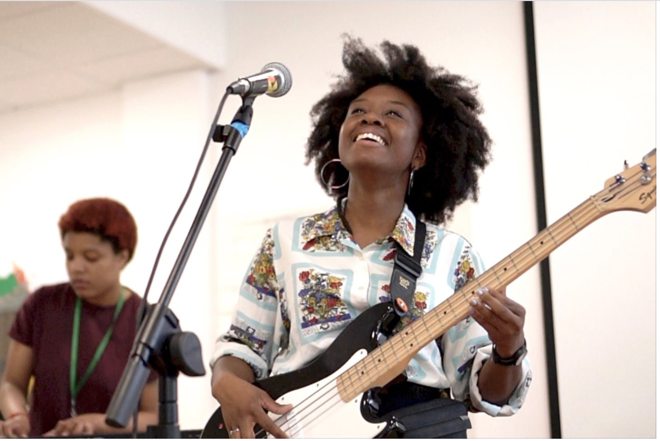 Black woman with bass smiles while playing