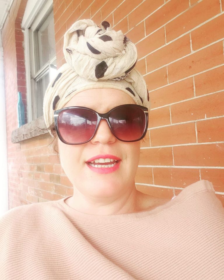 Woman in sunglasses and head wrap in front of a brick wall