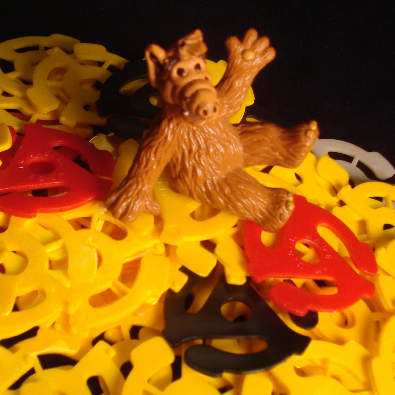Small Alf doll sitting on pile of plastic toy pieces waves to the camera
