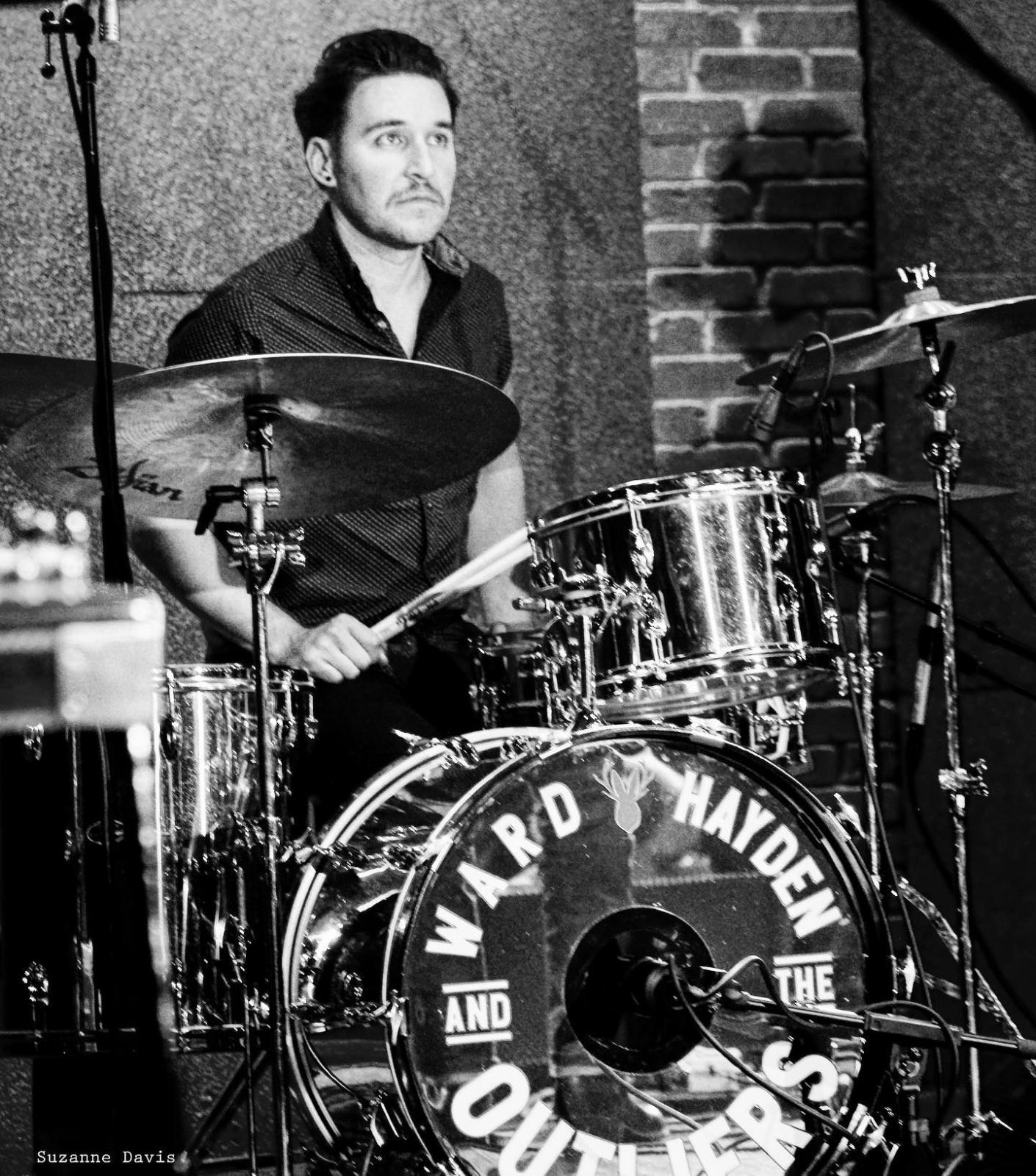 Manin button up tee plays drums in black and white image