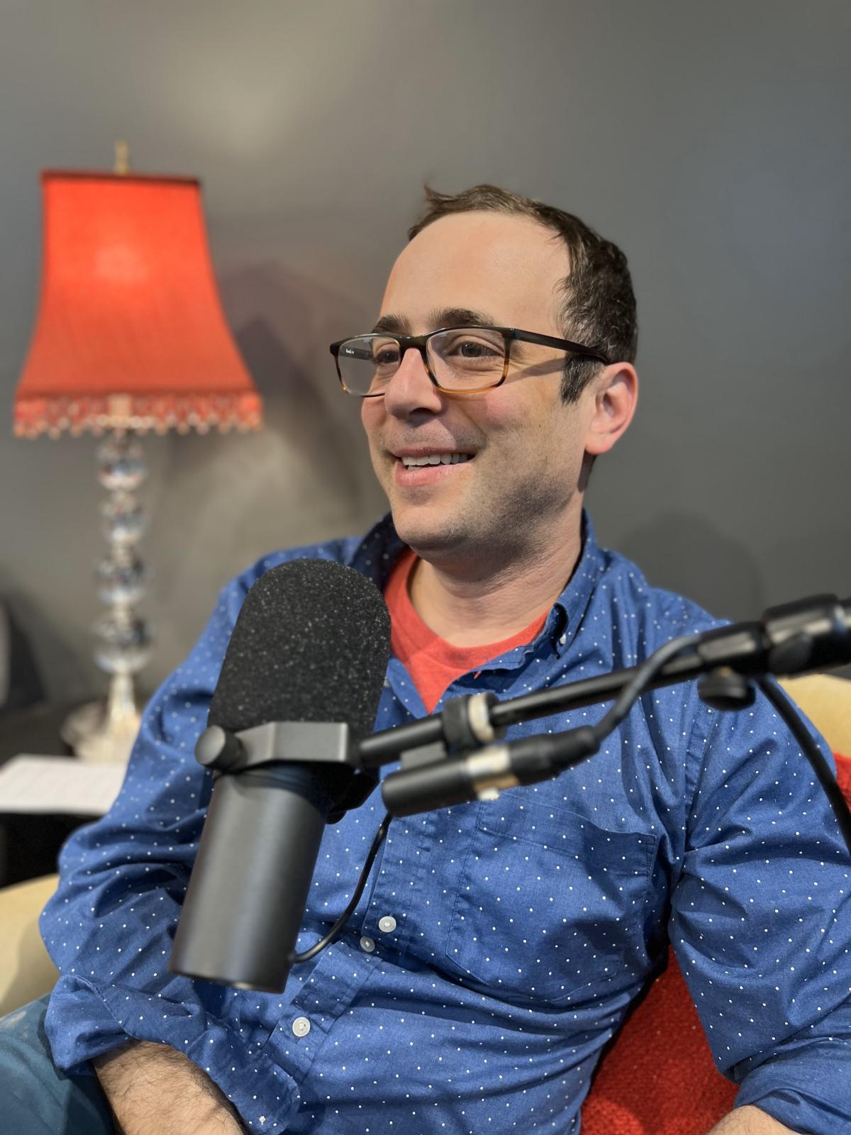 David is wearing a blue shirt and speaking into a microphone